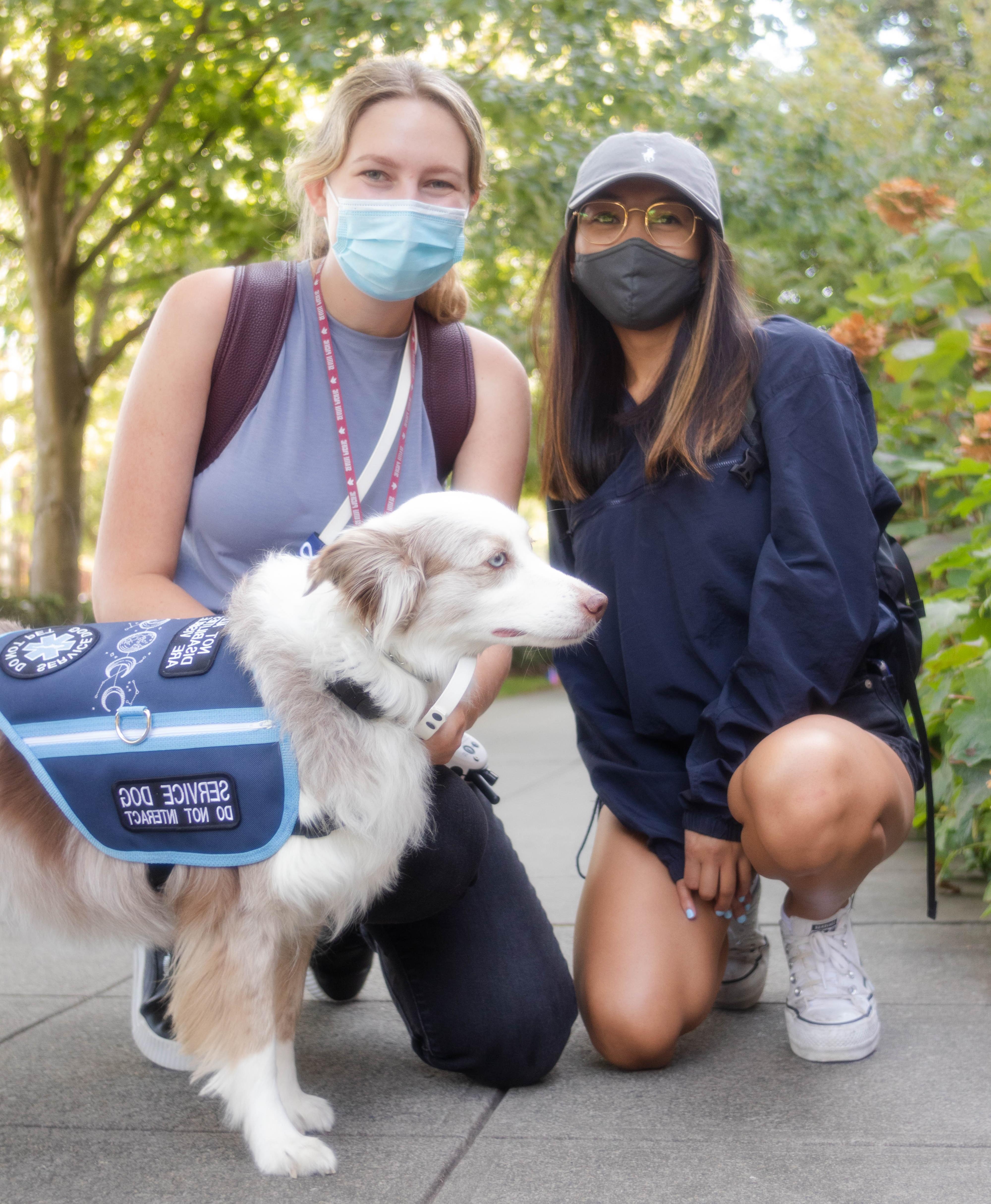 两个学生带着一只服务犬蹲在外面.